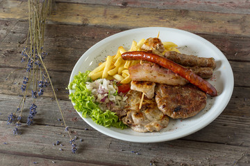 Balkan specialities - a plate of mixed meat including cevapi, pljeskavica, roasted pork neck and brisket.  on a wooden background. rustic food