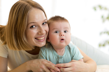 Mom and son lying down on bed in nursery room. Mother embracing infant baby.