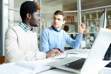 Portrait of two young business people, one of them African-American, working together in modern...
