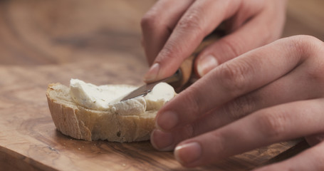 female hands spreading cream cheese on baguette slice