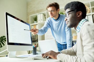 Portrait of two young web developers, one of them African,  discussing IT project pointing at code...