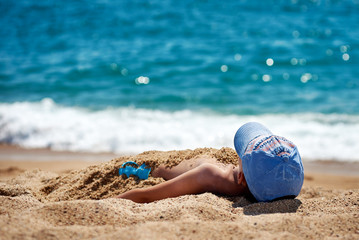 Boy strewed with the sand is laying on the beach.