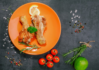 Grilled chicken legs with tomatoes and rosemary on a black plate on a stone,concrete  background