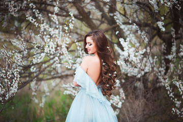 Happy beautiful young woman with long black healthy hair enjoy fresh flowers and sun light in blossom park at sunset.