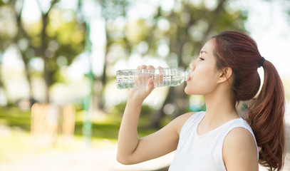 Young beautiful woman  drinking water at summer green park.