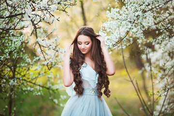 Happy beautiful young woman with long black healthy hair enjoy fresh flowers and sun light in blossom park at sunset.