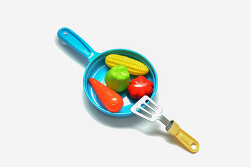 Children's plastic frying pan with vegetables on a white background