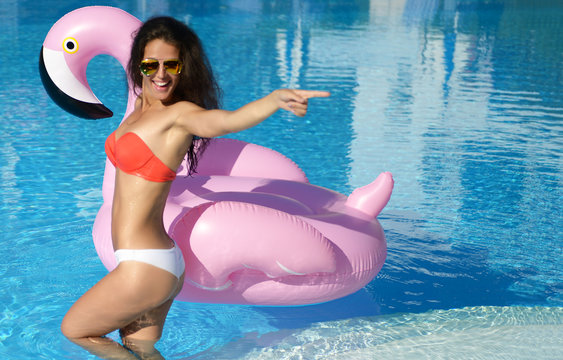 Woman in a swimming pool leisure on a giant inflatable giant pink flamingo float mattress in red bikini 
