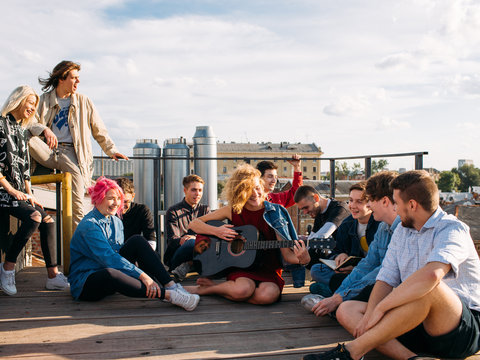 Relaxed smiling young people travel Europe. Sitting on a rooftop singing and enjoying their trip. Youth lifestyle