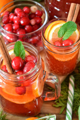 Punch with cranberries and orange decorated with mint and a stick of cinnamon in glass vessels