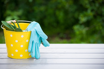 Yellow bucket with garden tools and Rubber blue safety gloves on the table in the garden. Hand...