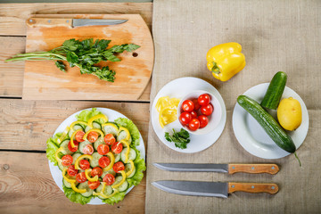 On a wooden background there are knives, a cutting board with greens plates with vegetables
