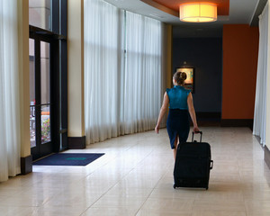 Fototapeta na wymiar Hotel Hall with Female Walking Pulling a Suitecase