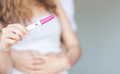 Selective focus happy couple hugging with positive pregnancy test in bedroom.