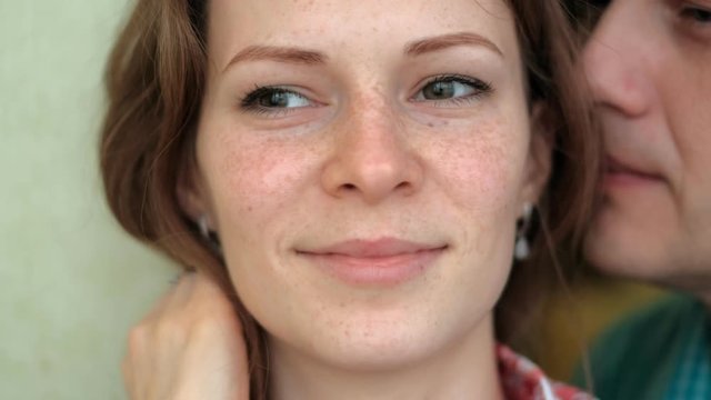 A man whispers in the ear of a woman, emotions on her face