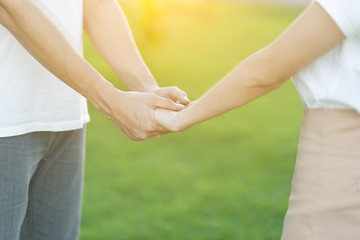 Lovers in the park tenderly hold hands together, blurred background.