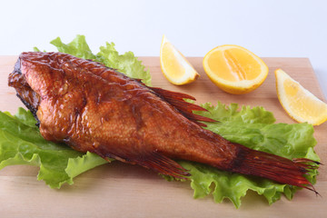 Smoked fish and lemon on green lettuce leaves on Wooden cutting board isolated on white background.