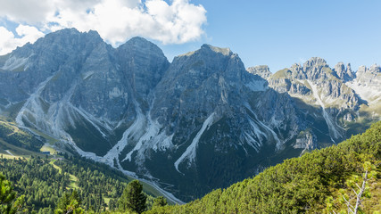 Sunny day in the European Alps. Mountain background with a green lush foreground. You can see the run off patterns in the mountainside. 