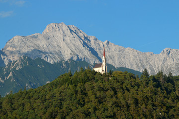 Church on a hill in a valley of the Austrian Alps The church sits among trees high above a roadway. The church has orange tile roofing and contrasts the greenery nicely.