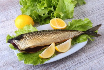 Smoked mackerele and lemon on green lettuce leaves on Wooden cutting board isolated on white background.