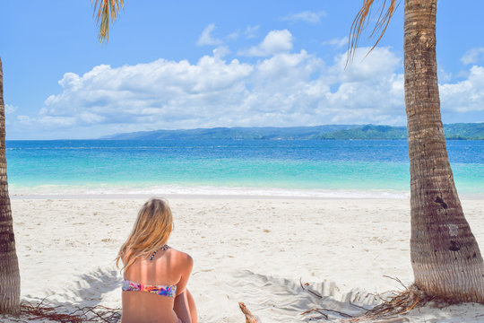 Frau sitzt im Bikini mit dem Rücken zur Kamera am weißen Sandstrand und schaut auf das Meer, Dominikanische Republik, Karibik, Samana