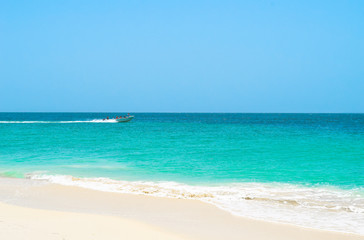 Fototapeta na wymiar Boot bringt Touristen zur Insel, im Vordergrund weißer Sandstrand, das türkisene Meer und der blaue Himmel, Motorboot im Hintergrund fährt auf Wasser