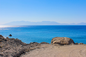 Fototapeta na wymiar Wunderschöner Ausblick auf das blaue türkisfarbene Meer, an Felsen entlang Ausblick auf den Ozean, am Horizont sieht man eine Insel