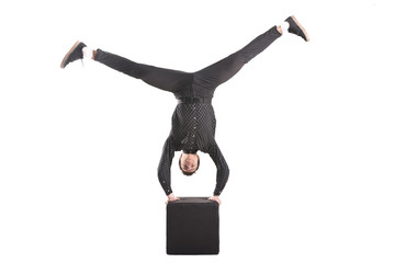 Guy performs stand upside down on the black cube isolated on white background