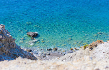 Aussicht auf das Meer einen Abhang hinunter auf Steine und Felsen im Wasser, türkisfarbenes blaues Meer, Wellen brechen an Steinen