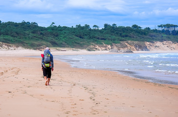 Pilgrim with backpack going on beach on the North way Camino de Santiago, Spain