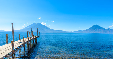 Wooden pier at Lake Atitlan on the beach in Panajachel, Guatemala. With beautiful landscape scenery of volcanoes Toliman, Atitlan and San Pedro in the background. Volcano Highland in Central America.