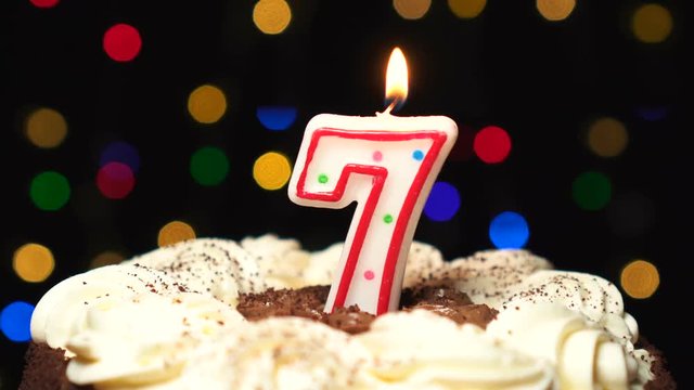 Number 7 on top of cake - seven birthday candle burning - blow out at the end. Color blurred background