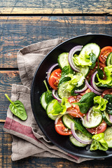 Healthy vegetable salad of fresh tomato, cucumber, spinach, onion and lettuce on plate. Diet menu. Top view.