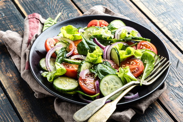 Healthy vegetable salad of fresh tomato, cucumber, spinach, onion and lettuce on plate. Diet menu