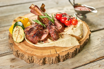 Roasted racks of beef with vegetables. Prepared roasted racks of beef with vegetables on lavash on wooden plate.