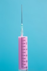 Close-up of medical syringe with pink medicine on blue background. Health care, medicine and pharmacy concept