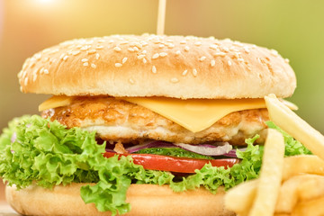 Close-up of a fast food burger containing meat topped with cheese, tomatoes, lettuce and onion. Fastfood close up.