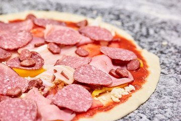 Close up sausage slices on pizza dough. Salami and ham on unbaked pizza.