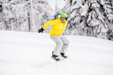 Fototapeta na wymiar Man in colorful sports clothes riding the snowboard on the snowy mountains with beautiful trees on the background