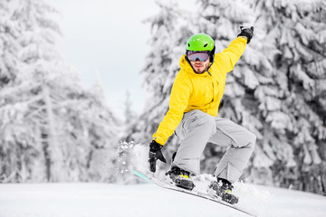 Fototapeta na wymiar Man in colorful sports clothes jumping with snowboard on the snowy mountains with beautiful trees on the background
