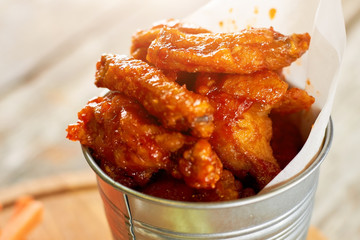 Juicy fried chicken meat pieces in sause, close up. Closeup hot chicken wings in aluminium bucket.