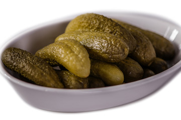 green pickled marinated gherkins in a white dish on wood table