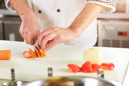 Cooker man slicing carrot using knife. Chef hands using knife. Slicing action.