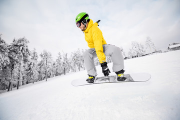 Man in colorful sports clothes riding the snowboard on the snowy mountains with beautiful trees on...