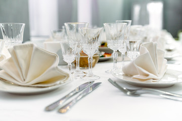 Luxury dinner set arranged on a table with vintage cream lace tablecloth and napkins, elegant porcelain dishes, silverware and crystal glassware