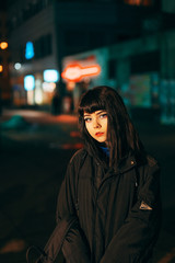 Young Japanese girl stand near neon lights and pose to the camera. Red and blue light, night time, street