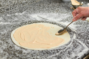 Spoon smearing pizza dough basis with creamy white sauce. Hand smearing sauce using spoon. Second...