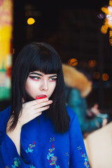 Young Japanese girl stand near neon lights and pose to the camera. Red and blue light, night time, street