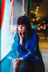 Young Japanese girl stand near neon lights and pose to the camera. Red and blue light, night time, street