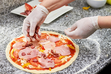 Obraz na płótnie Canvas Sprinkling hunt sausage slices onto pizza. Adding sausages to pizza.